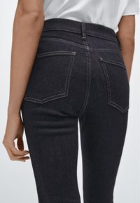 Černé džíny z denimu s vysokým pasem, které mají přiléhavý střih, zadní kapsy a kontrastní šití. Hladká textura se slabým pružením.