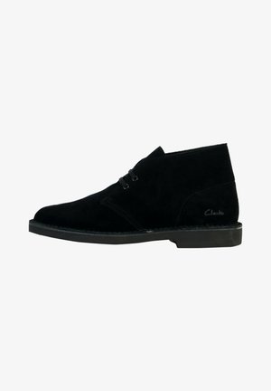 Schwarze Wildleder-Ankelboots im Chukka-Design, mit zwei Schnürösen und einer flachen Gummisohle. Markenname "Clarks" auf der Seite sichtbar.