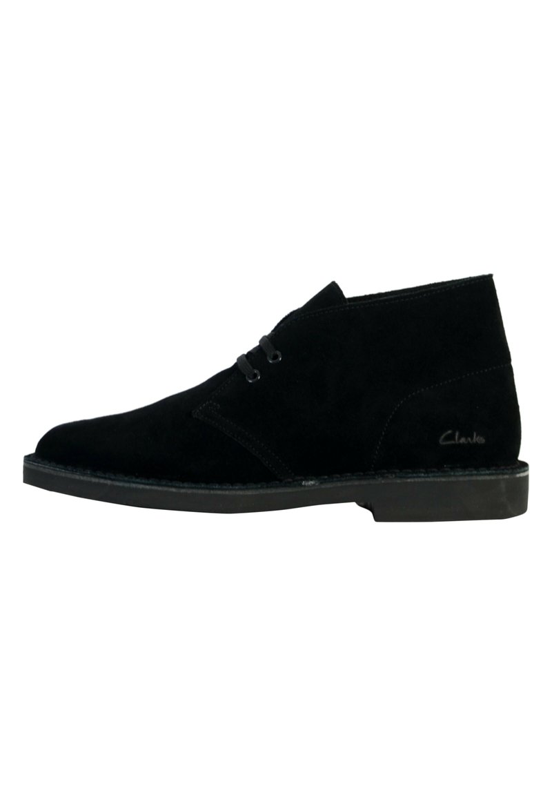Botas de tobillo de gamuza negra con diseño chukka, que incluyen dos ojales para los cordones y una suela plana de goma. El nombre de la marca "Clarks" es visible en el lado.