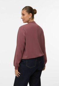 Bordeauxrode blouse met lange mouwen en een losse pasvorm, voorzien van een ronde halslijn. Gecombineerd met donkere denim broek. Gladde stoftextuur.