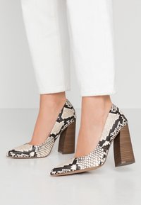 Escarpins avec un motif serpent noir et blanc, bout pointu, surface texturée et talons en bois épais.