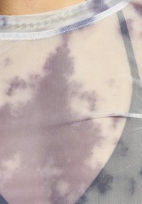 Mrežasta majica z lahkim vijoličnim tie-dye vzorcem, ki ima okroglo izreznico in kontrastne obrobe. Tkanina ima mehak, prosojen izgled.