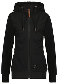 Giacca nera con zip e cappuccio, dotata di cordini, polsini e orlo a costine, tasche laterali con bottoni e un piccolo emblema metallico a forma di cuore sulla parte anteriore.
