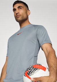 Hallide hallide lühikeste varrukatega hall Nike spordipaita, kus on must-valge jalgpall punaste aktsentidega.