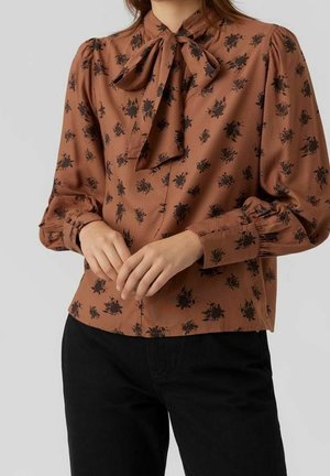 Braune Bluse mit Kragen und Schleife, mit schwarzem Blumenmuster, langen puffärmel und Knopfleiste. Strukturierter Stoff.
