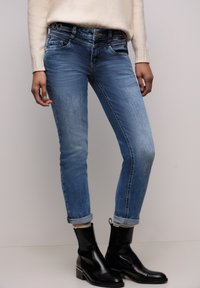 Jean en denim bleu taille haute avec une coupe slim, équipé de revers retroussés, de détails cousus et d'un design à cinq poches. Porté avec des bottines noires.