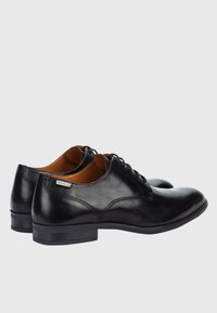 Chaussures habillées en cuir noir avec une finition lisse, un design à lacets et une doublure intérieure marron. Elles présentent un petit talon et des détails de couture discrets.