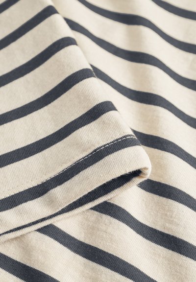 Gros plan sur un tissu beige avec des rayures horizontales bleu foncé espacées régulièrement et une couture visible sur le bord plié.