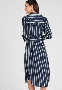 Vestito camicia blu navy con strisce verticali verdi e bianche. Presenta un colletto, maniche lunghe e una cintura annodata in vita.