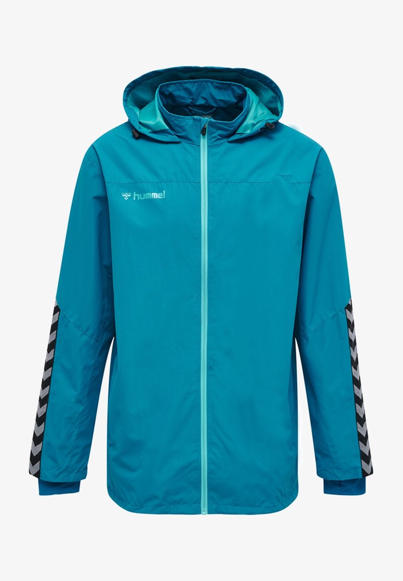 Veste coupe-vent bleue à capuche avec fermeture éclair à l'avant, bandes chevrons noires et grises sur les manches, et logo "hummel" sur la poitrine.