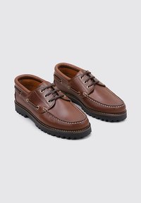 Zapatos de cuero marrón con diseño de cordones, puntera redondeada y costuras en contraste. Suela de goma gruesa con tracción. Textura suave y acentos mínimos.