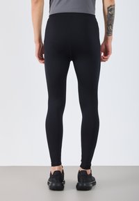 Fekete leggings, testsimuló fazonnal és sima textúrával, magas derékkal. Fekete sportcipővel viselve.