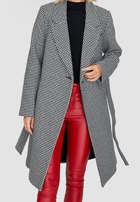 Zwart-wit houndstooth-gepatenteerd overjas met een getailleerde pasvorm, grote revers en een soepele textuur, gecombineerd met rode neplederen broek.