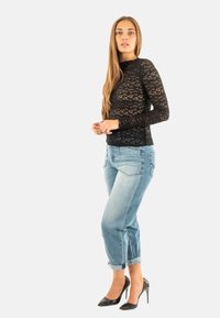 Top lungo a maniche in pizzo nero abbinato a jeans celesti arrotolati e tacchi alti neri. Il top presenta un design a maglia aperta e testurizzata.