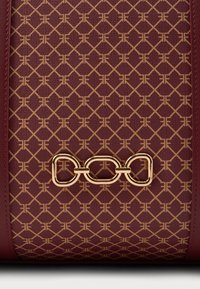 Borsa a mano in tela bordeaux con motivo geometrico in oro embossato e dettaglio chain in oro. Texture liscia con forma strutturata. Ampio scomparto principale.