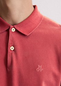Rød polo-skjorte med klassisk krage og to knapper. Har en liten brodert logo "M OP" nær kanten. Mykt, strukturert stoff.