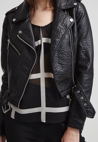 Svart konstläderbikerjacka med en texturerad yta, silverfärgade dragkedjor och tryckknappdetaljer. Har en asymmetrisk design.