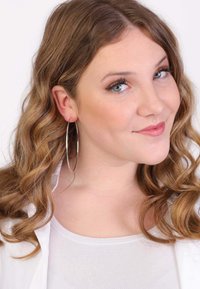 Grote zilveren creolen, losjes hangend, gecombineerd met een witte top. De persoon heeft golvend, schouderlang haar en een natuurlijke make-up.