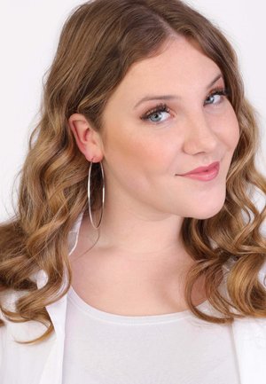 Grote zilveren creolen, losjes hangend, gecombineerd met een witte top. De persoon heeft golvend, schouderlang haar en een natuurlijke make-up.