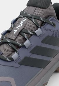 Chaussure Terrex gris foncé avec une tige en maille, des accents en caoutchouc, des lacets contrastés et des panneaux texturés pour une traction et une durabilité.