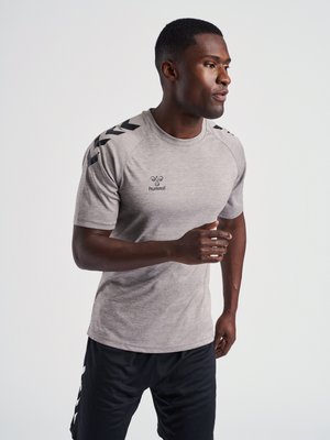 Man in gray Hummel sports t-shirt and black shorts appears to be jogging or running against a plain light background.