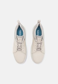 Helle beige Sneaker mit einem glatten Leder-Obermaterial, textile Akzenten, gepolstertem Kragen und weißer Gummisohle. Verfügt über ein zentrales Schnürsystem.