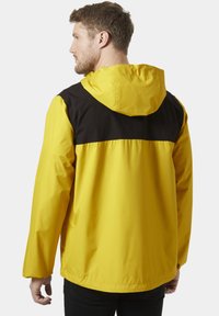 Chaqueta impermeable amarilla con una sección superior negra, equipada con capucha y puños elásticos, con una textura suave y duradera.