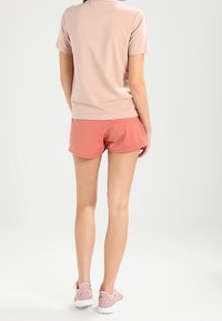 Jasnoróżowa, krótko rękawowa koszulka zestawiona z koralowymi szortami. Oba elementy wykonane są z miękkich materiałów. Obuwie to różowe, fakturowane sneakersy.