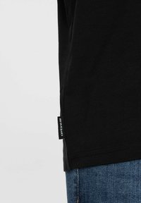 Sort bomulds T-shirt med korte ærmer, prydet med et side-tag mærket "ombre" og en regular fit, parret med blå denim jeans.