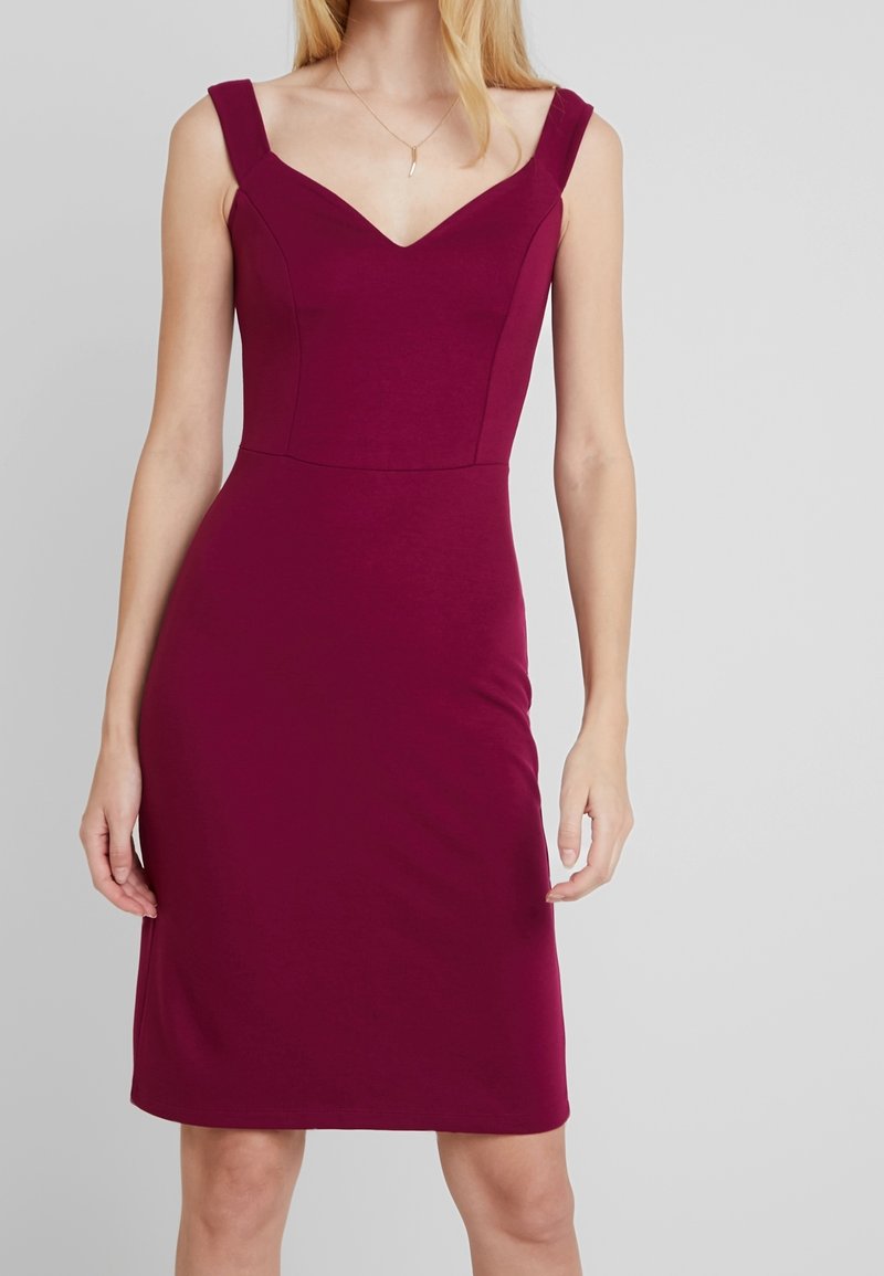 Robe sans manches magenta foncé avec de larges bretelles et un décolleté en V, portée par une personne aux longs cheveux blonds et un collier pendentif en argent.