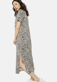 Maxikleid mit Leopardenmuster, kurzen Ärmeln, seitlichem Schlitz, aus leichtem Stoff, mit weißem Hintergrund und braunen sowie schwarzen Flecken.