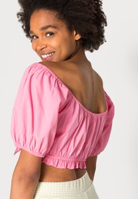 Blusa cropped rosa com mangas bufantes e cintura elástica, apresentando um decote largo e um tecido ligeiramente texturizado.