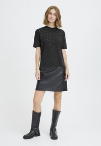 Sort t-shirt med sølvnitter foran, kombineret med en sort lædernederdel og sort knælange støvler.