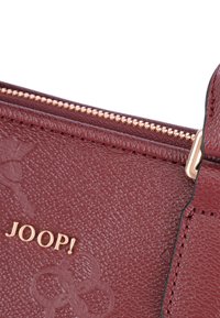 Bordeaux struktureret lædertaske med guldfarvet hardware; har en lynlåslukning og prægede logo "JOOP!" på fronten.