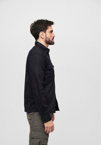 Black long-sleeve shirt with button-up front, side pocket, and collar. Worn with olive green cargo pants featuring multiple pockets.