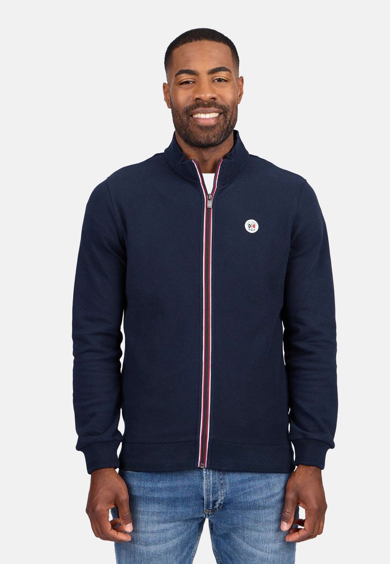 Sweat-shirt zippé marine avec des poignets et un ourlet côtes, arborant un emblème blanc et un accent rayé rouge et blanc le long de la fermeture éclair.