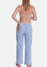 Jean ample en denim bleu clair avec taille haute, doté de deux poches arrière et d'une petite étiquette de marque. La texture semble douce et décontractée.