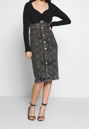 Musta pitkähihainen paita yhdistettynä istuvaan, nappikiinnitteiseen farkkuhameeseen, jossa on pystysaumat ja kynsilinjainen siluetti riehumalla. 