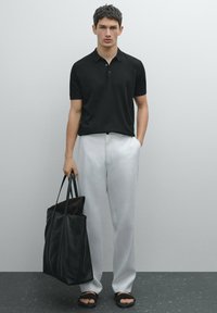 Maglietta polo nera, pantaloni bianchi larghi, borsa a tracolla in pelle nera e sandali neri. Tessuto liscio, design semplice e colori neutri.
