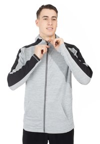 Grå zip-up hættejakke med sorte detaljer, tekstureret stof, to forlommer og tætsiddende manchetter; modellen justerer lynlåsen.