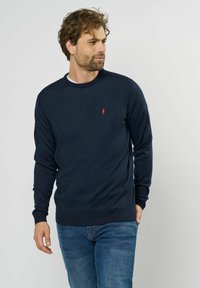 Marineblauer Strickpullover mit Rundhalsausschnitt und langen Ärmeln. Verfügt über ein kleines rotes Logo auf der Brust sowie gerippte Bündchen und Saum.