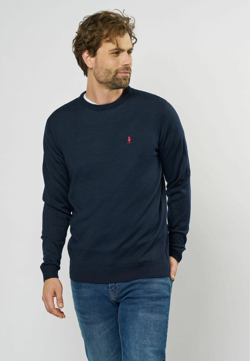 Marineblauer Strickpullover mit Rundhalsausschnitt und langen Ärmeln. Verfügt über ein kleines rotes Logo auf der Brust sowie gerippte Bündchen und Saum.