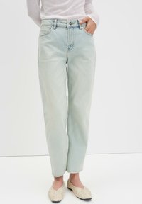 Hellblaue Jeans mit hoher Taille, geraden Beinen, zwei vorderen Taschen und subtilen Abnutzungen. Kombiniert mit cremefarbenen Halbschuhen.