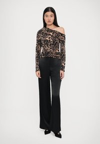 Top a maniche lunghe con stampa leopardata, con una spalla scoperta, abbinato a pantaloni neri a vita alta e gamba larga, tutti realizzati in un tessuto liscio.