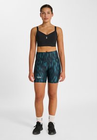 Schwarzer Sport-BH und kurze Shorts mit türkisfarbenem Muster. Die Shorts haben eine glatte Textur und einen hohen Bund, mit einem Logo am unteren Bein.