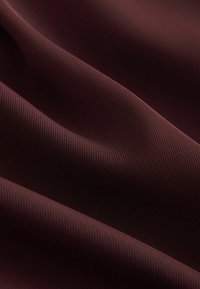 Burgundská tkanina s hladkou textúrou, so subtilným ryhovaním. Materiál sa zdá byť ľahký a flexibilný, ideálny pre rôzne aplikácie.