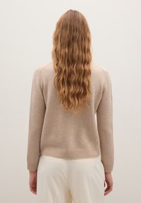 Beige Strickpullover mit langen Ärmeln, gerippten Bündchen und Saum, weicher Textur, über hellen Hosen getragen, von hinten betrachtet.