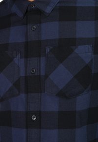 Chemise à carreaux bleu marine et noire en flanelle, avec un bouton, un col et deux poches poitrine.