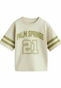 Camiseta de algodón color beige claro con el texto "PALM SPRINGS" y el número "21" en verde oliva. Presenta mangas cortas y acentos a rayas en las mangas.