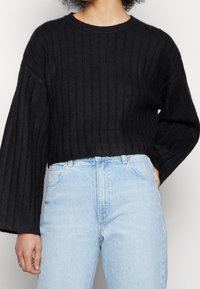 Czarny krótki sweter o prążkowanej strukturze i szerokich rękawach, połączony z jasnoniebieskimi dżinsami o wysokim stanie. Prosty krój z okrągłym dekoltem.